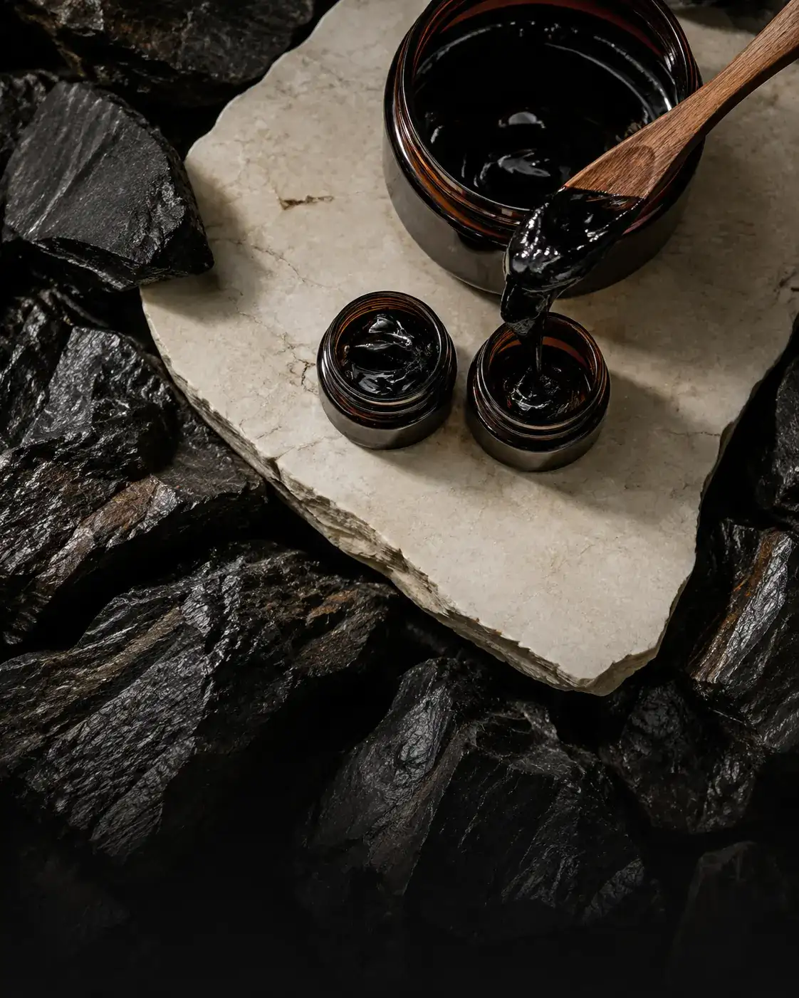 Dark shilajit resin being portioned into unbranded amber jars.