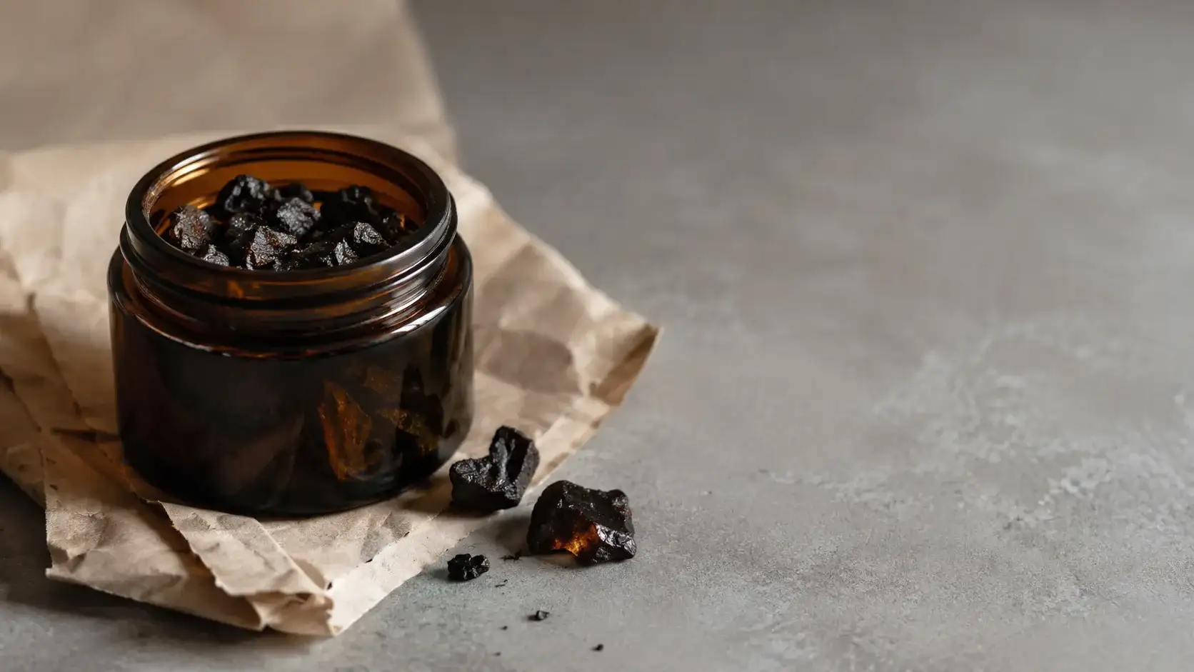 An unbranded amber glass jar of dark resin resting on plain kraft packaging paper on a cool grey surface.