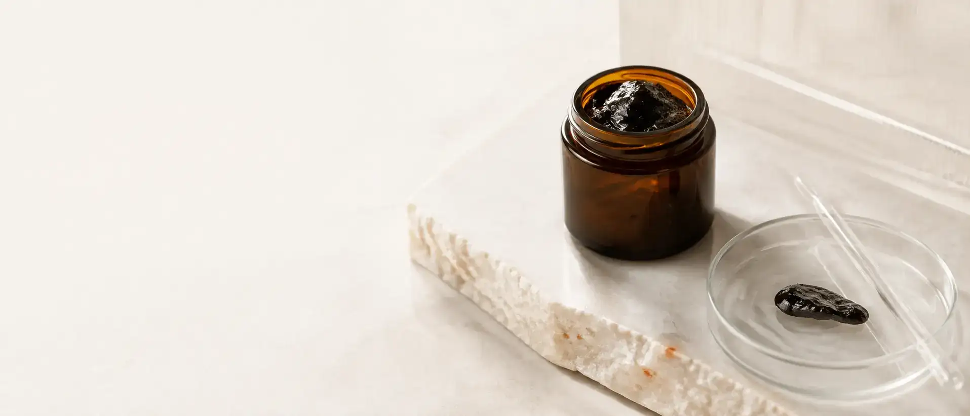 An unbranded amber jar and a measured resin sample on pale mineral stone.