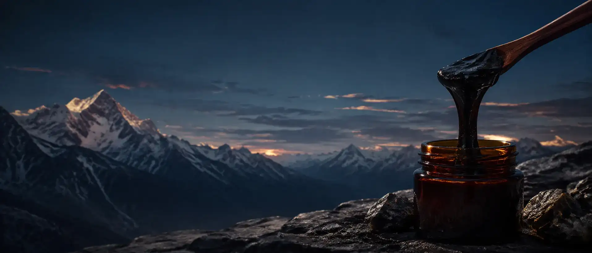 An amber jar of dark resin among mineral rock beneath blue-hour Himalayan peaks.