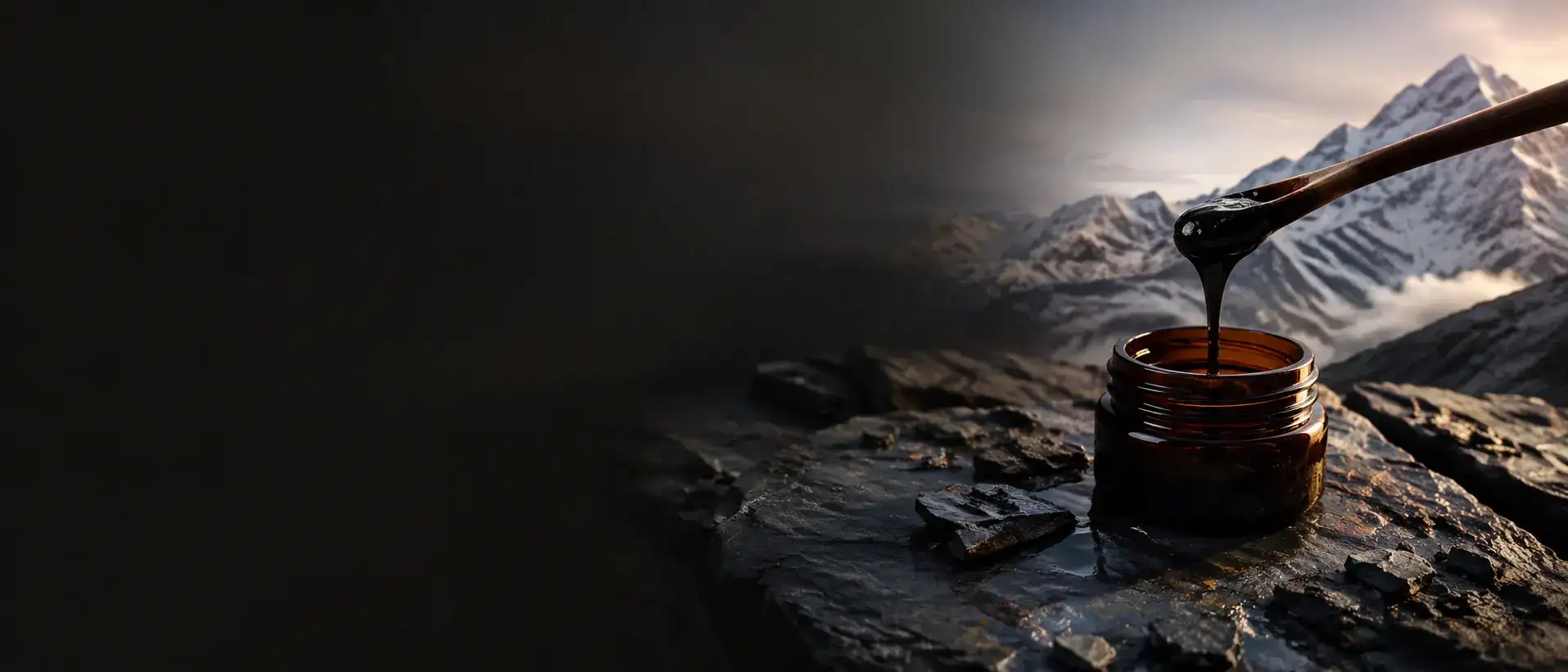 Dark shilajit resin flowing from a wooden spoon into amber glass above Himalayan rock.